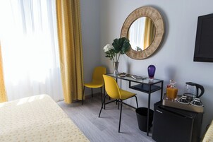 Una camera d'albergo con un letto, una scrivania con una sedia, un piccolo frigorifero, una macchina per il caffè e uno specchio a parete.