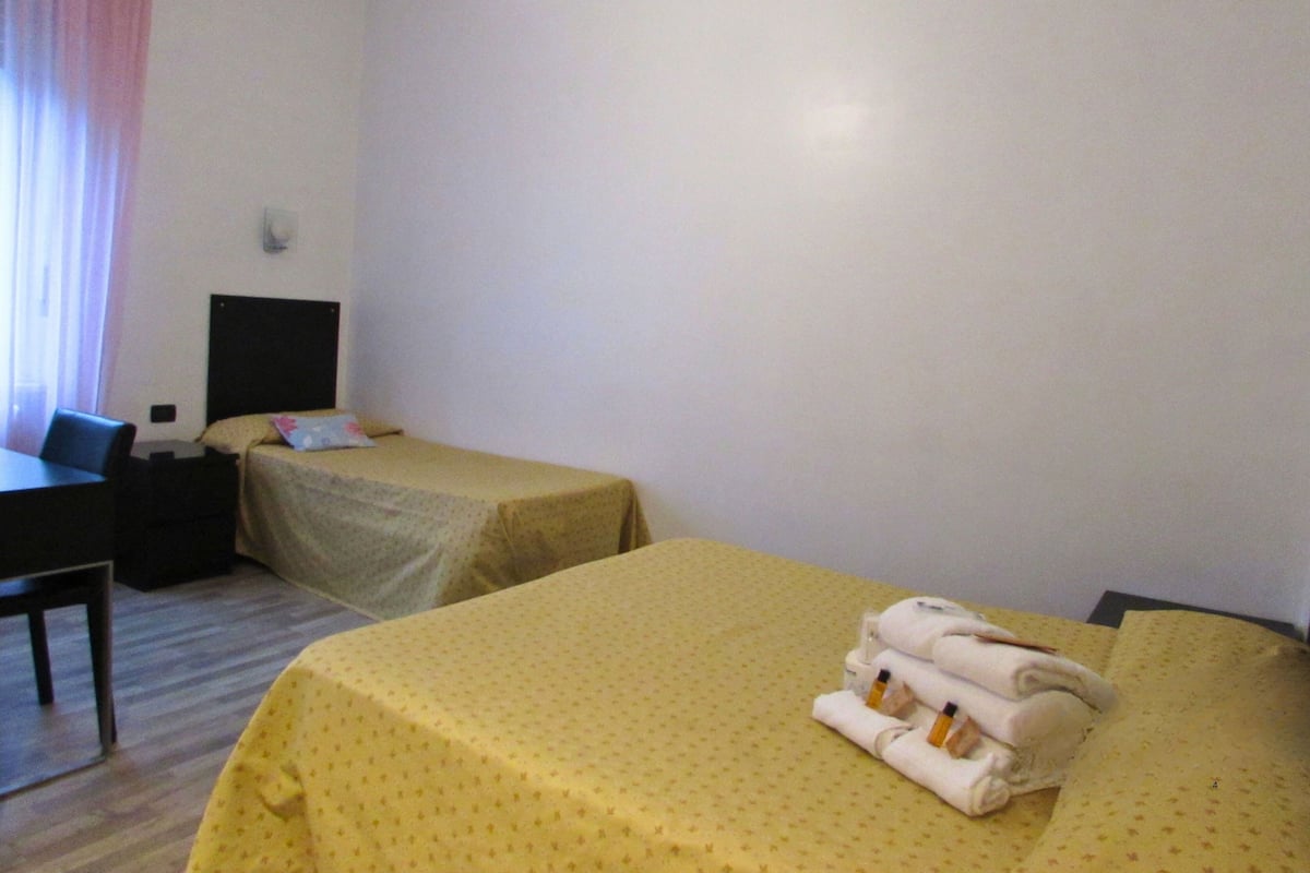 A hotel room with two single beds, a desk, a chair, and a nightstand.
