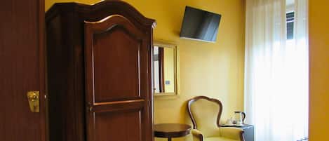 Une pièce avec une porte en bois, une table ronde avec une chaise, un téléviseur à écran plat fixé au mur et une fenêtre avec des rideaux.