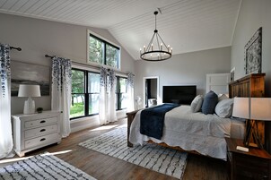 Un dormitorio con una cama grande, televisión, cómoda de madera y ventana con cortinas.