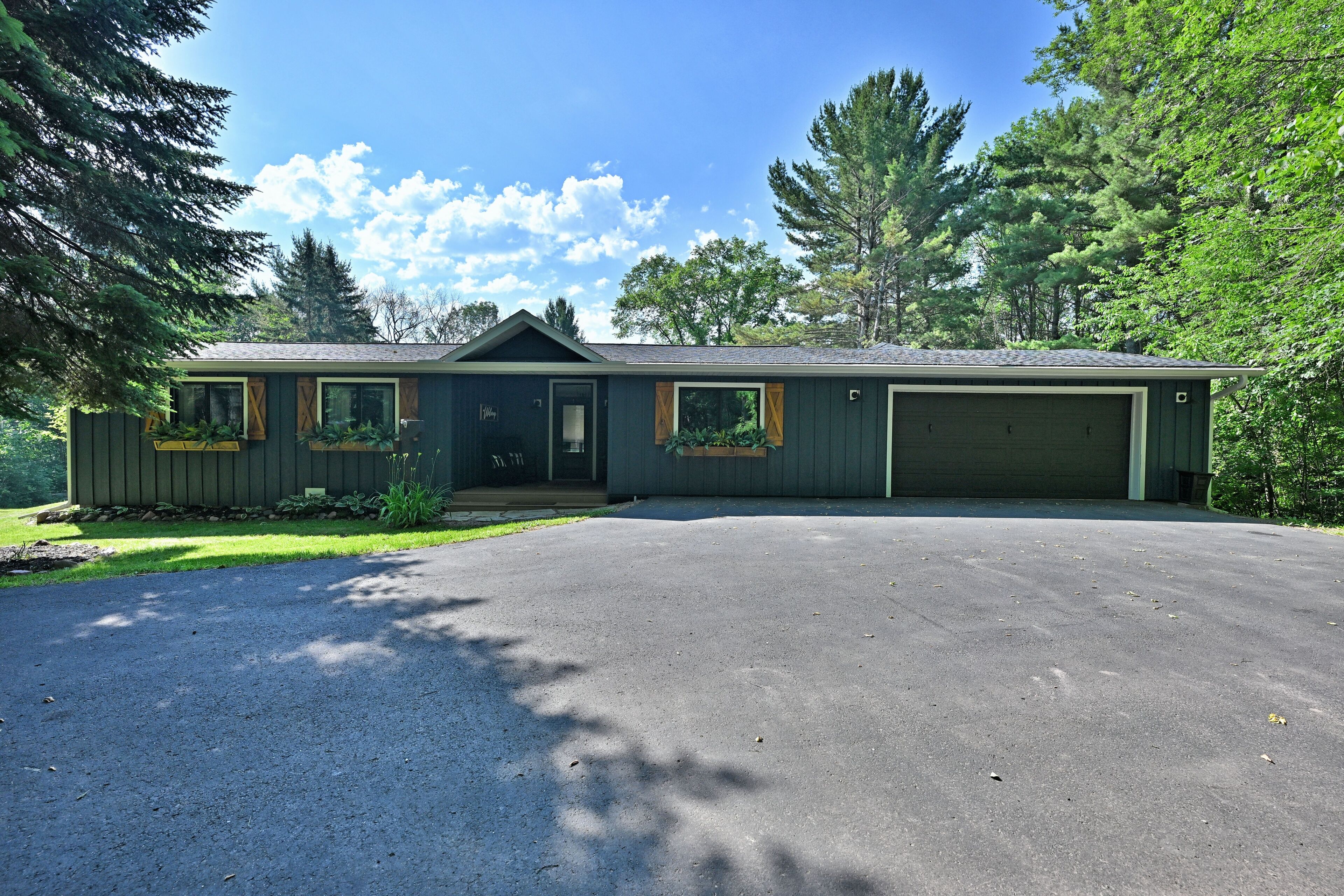 A single-story house with a garage, surrounded by trees and a clear sky.