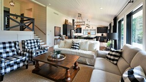 A spacious living room with a sofa, armchairs, and a coffee table. A staircase leads to an upper level.
