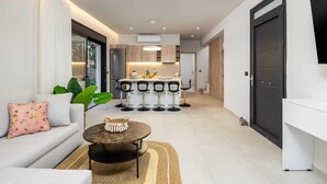 A modern living room with a sofa, coffee table, and a kitchen area with bar stools. - Terra Magna - Alba Villa (Rhodes)