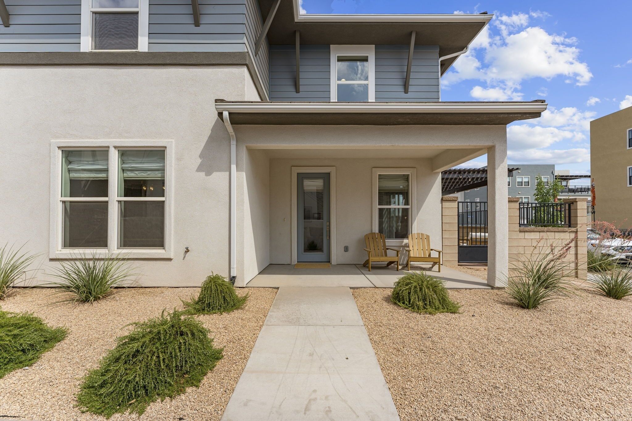 A two-story house with a covered porch, a front door, and a small seating area with two chairs.