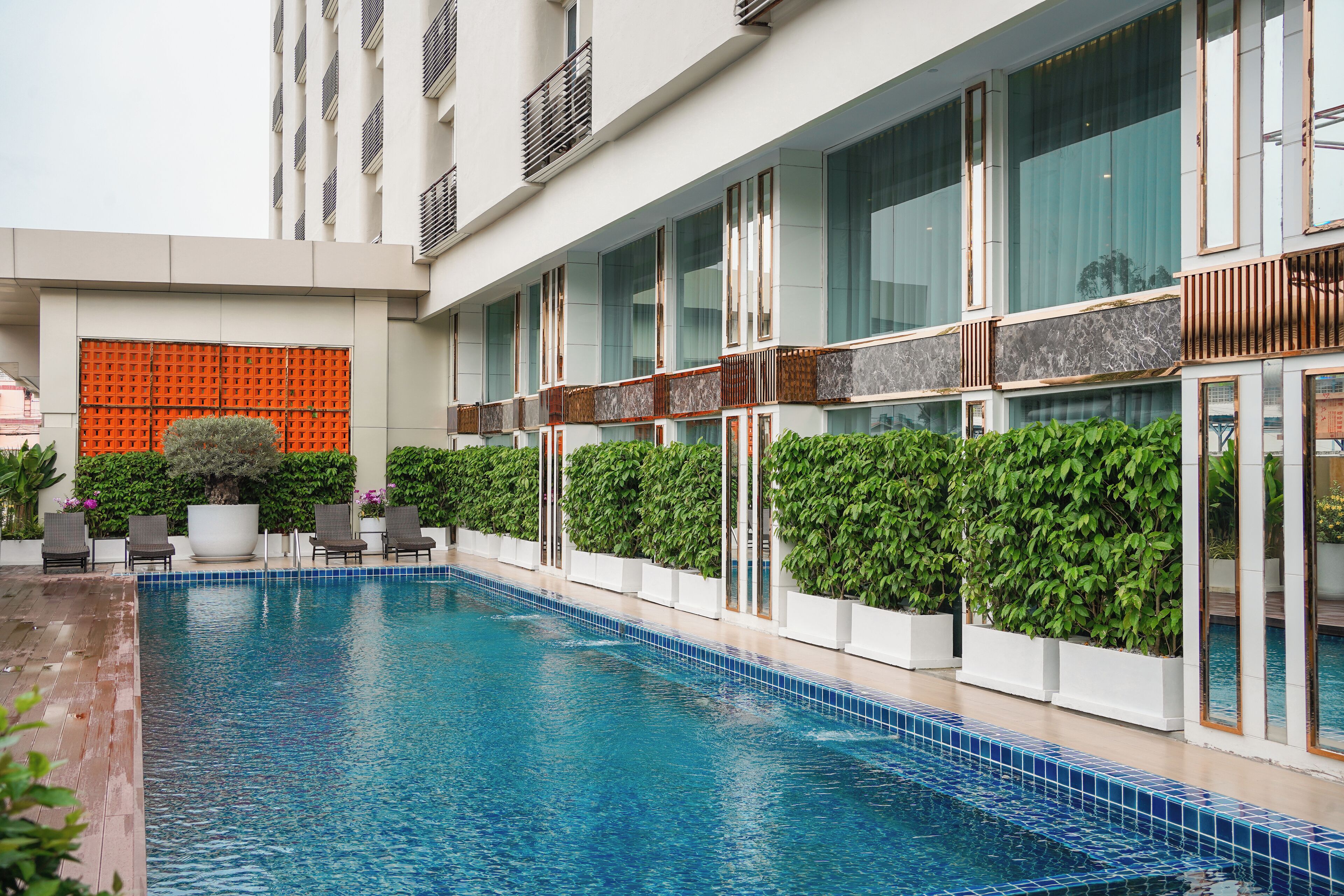 A swimming pool with a tiled edge, surrounded by potted plants and outdoor seating.