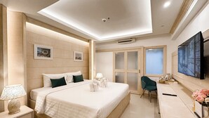 A hotel room with a large bed, bedside tables, a desk with a chair, a flat-screen TV, and a sliding door leading to a bathroom. - Golden Empire Suvarnabhumi Hotel (Bang Phli)