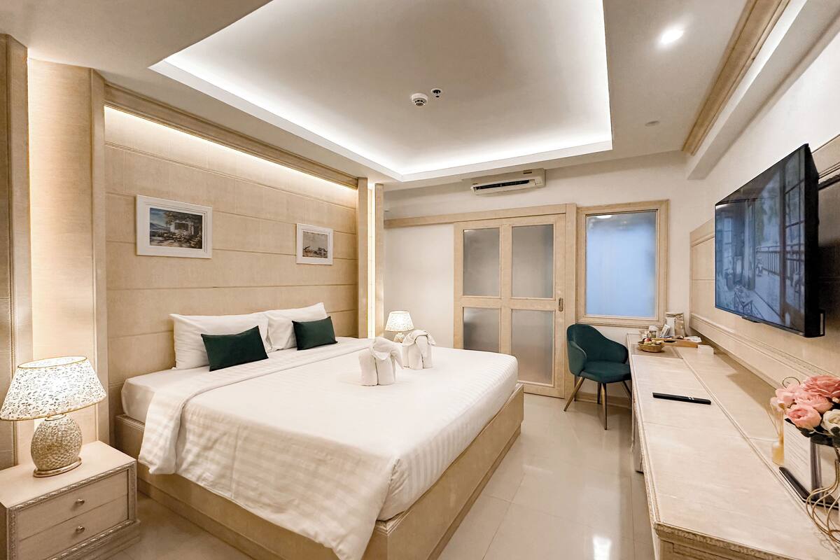 A hotel room with a large bed, bedside tables, a desk with a chair, a flat-screen TV, and a sliding door leading to a bathroom.