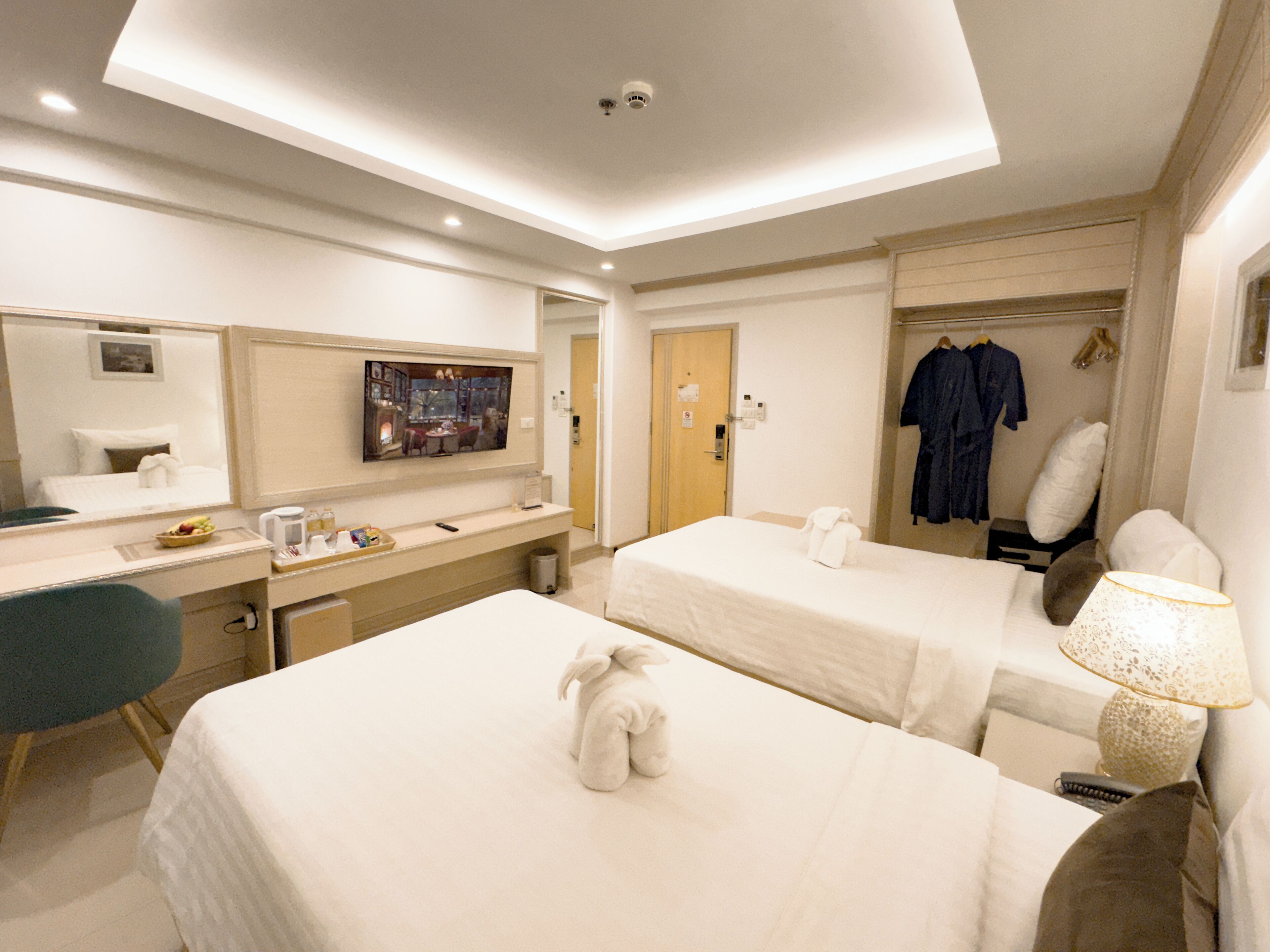 A hotel room with two beds, a desk, a chair, a TV, and a robe rack.