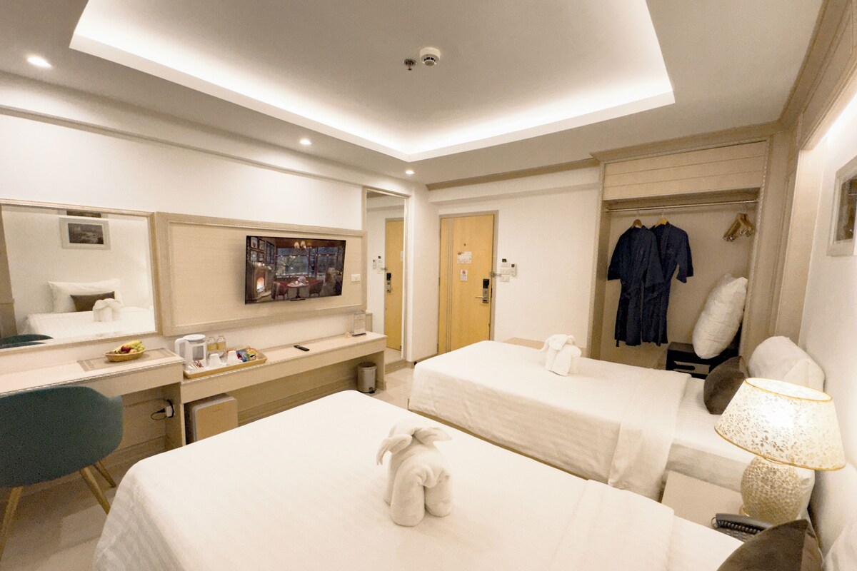 Una habitación de hotel con dos camas, un escritorio, una silla, un televisor y un perchero para bata.