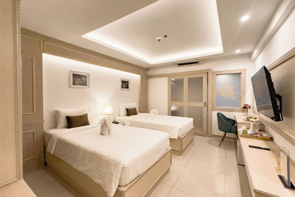 A hotel room with two beds, a desk with a chair, a TV, and a sliding door.