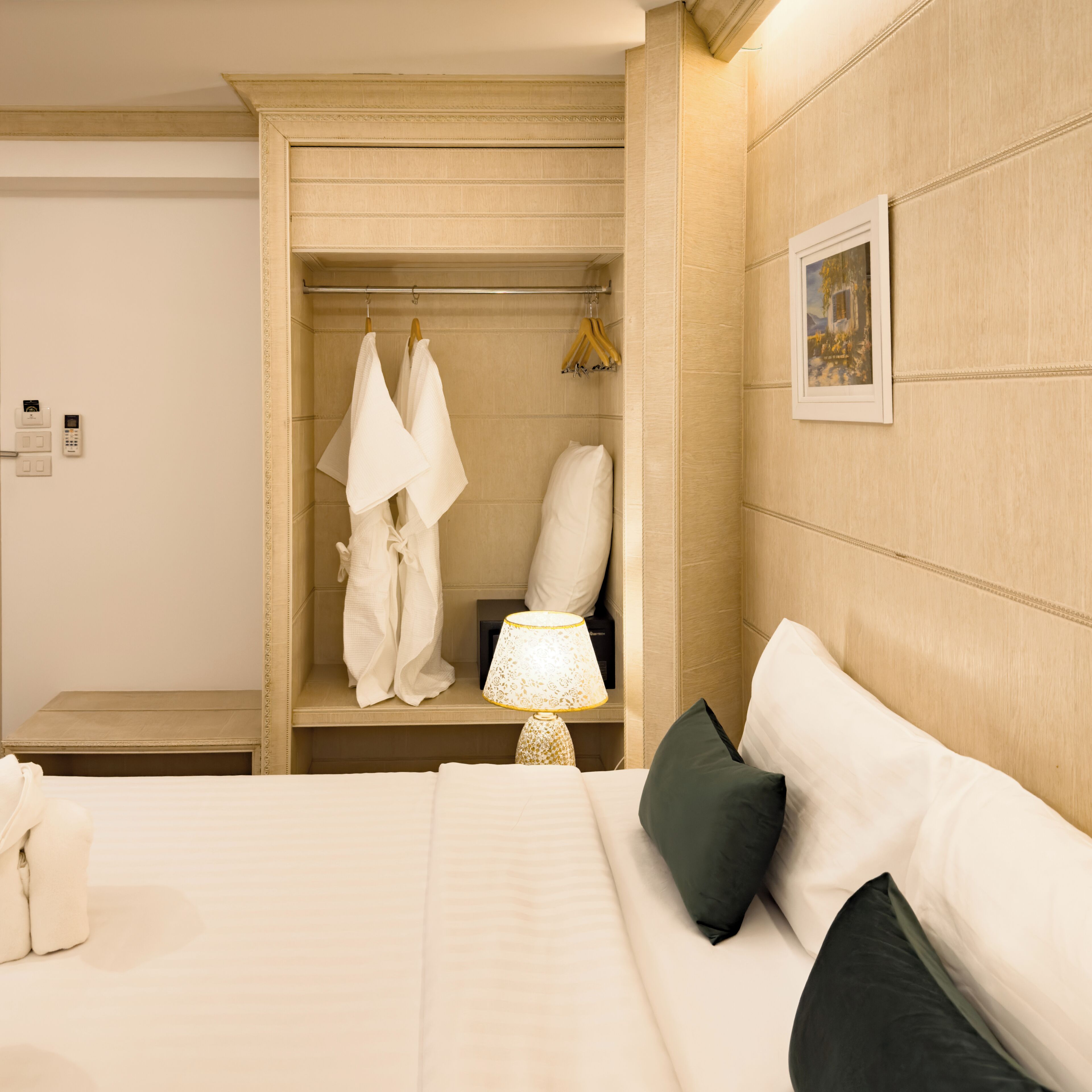 Habitación de hotel con cama, mesita de noche, lámpara, armario y un cuadro en la pared.