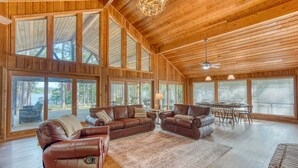 A spacious living room with leather sofas, a dining area, and large windows offering views of the outdoors.