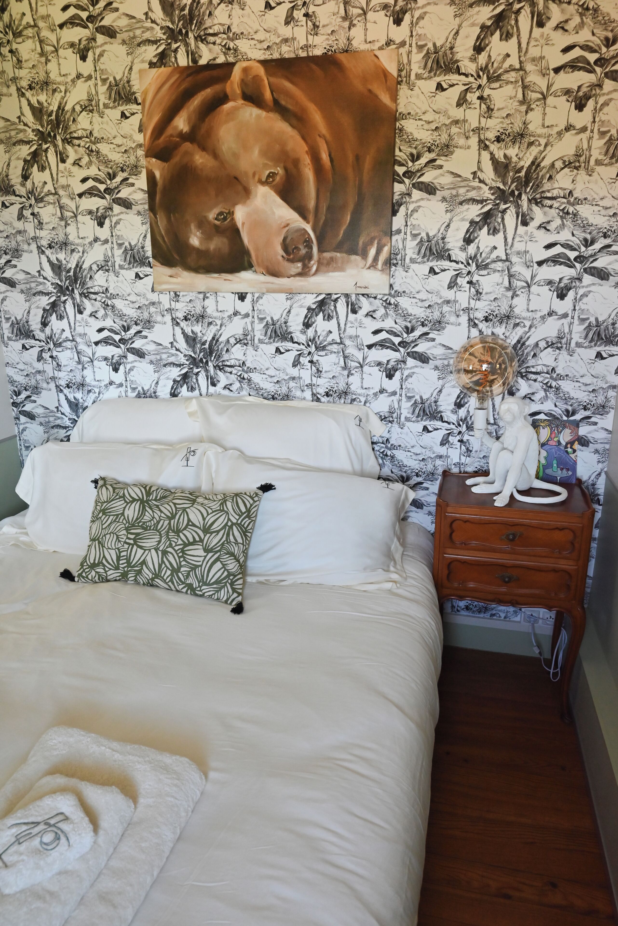 A bedroom with a bed, pillows, a nightstand, a wall tapestry, and a fan.