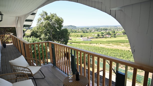 A balcony with wicker furniture, a bottle of wine, and a view of a vineyard.