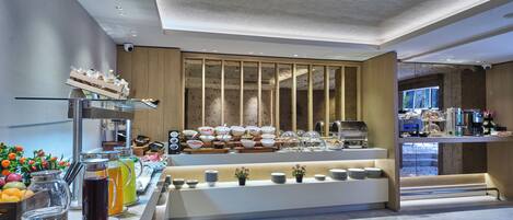 Ein modernes Frühstücksbuffet mit vielfältigen Speisen, einer Kaffeestation und einer Sitzgelegenheit mit Aussicht.