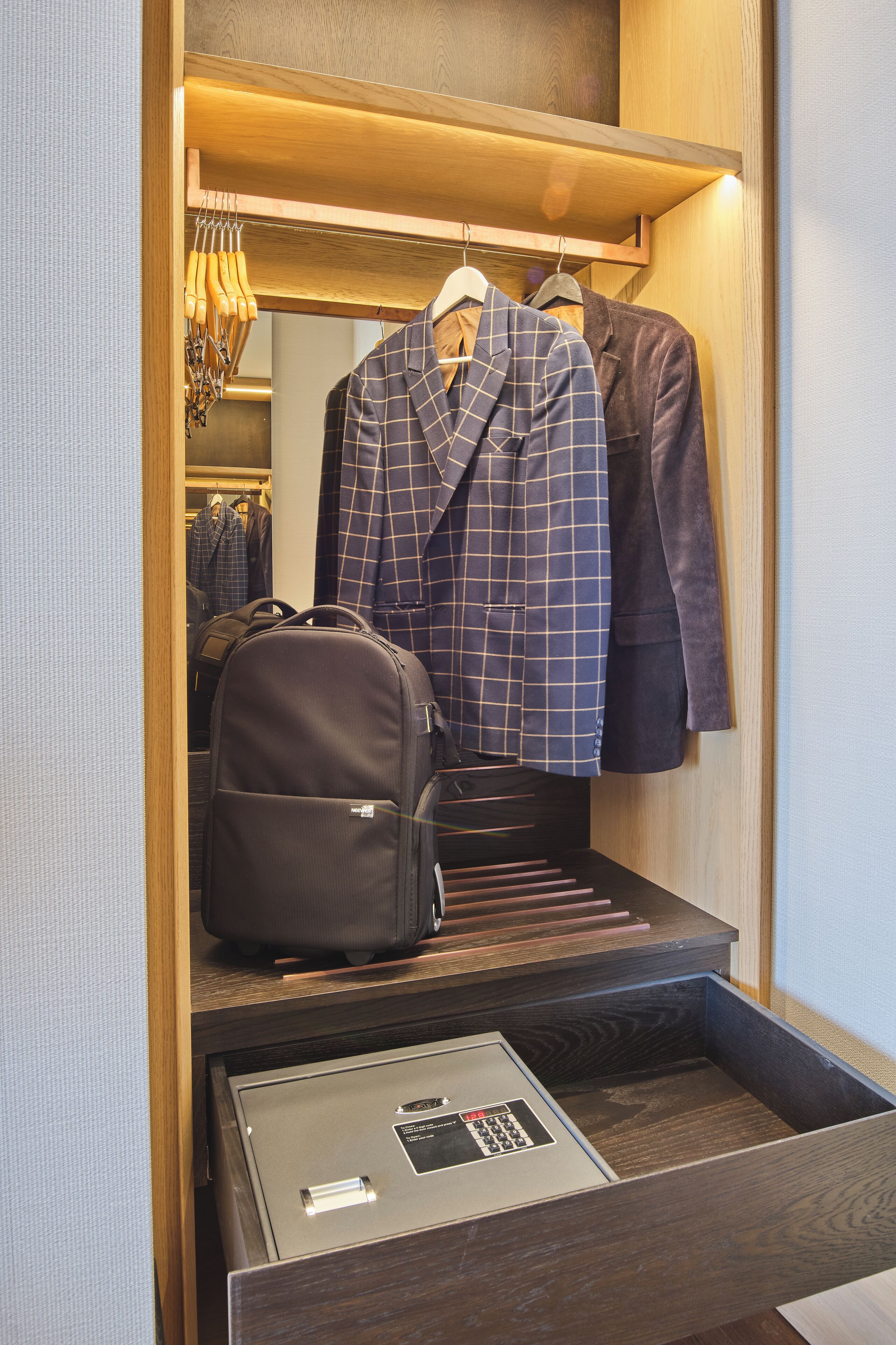 Een houten garderobe met een kledingroede, een koffer en een kluis.