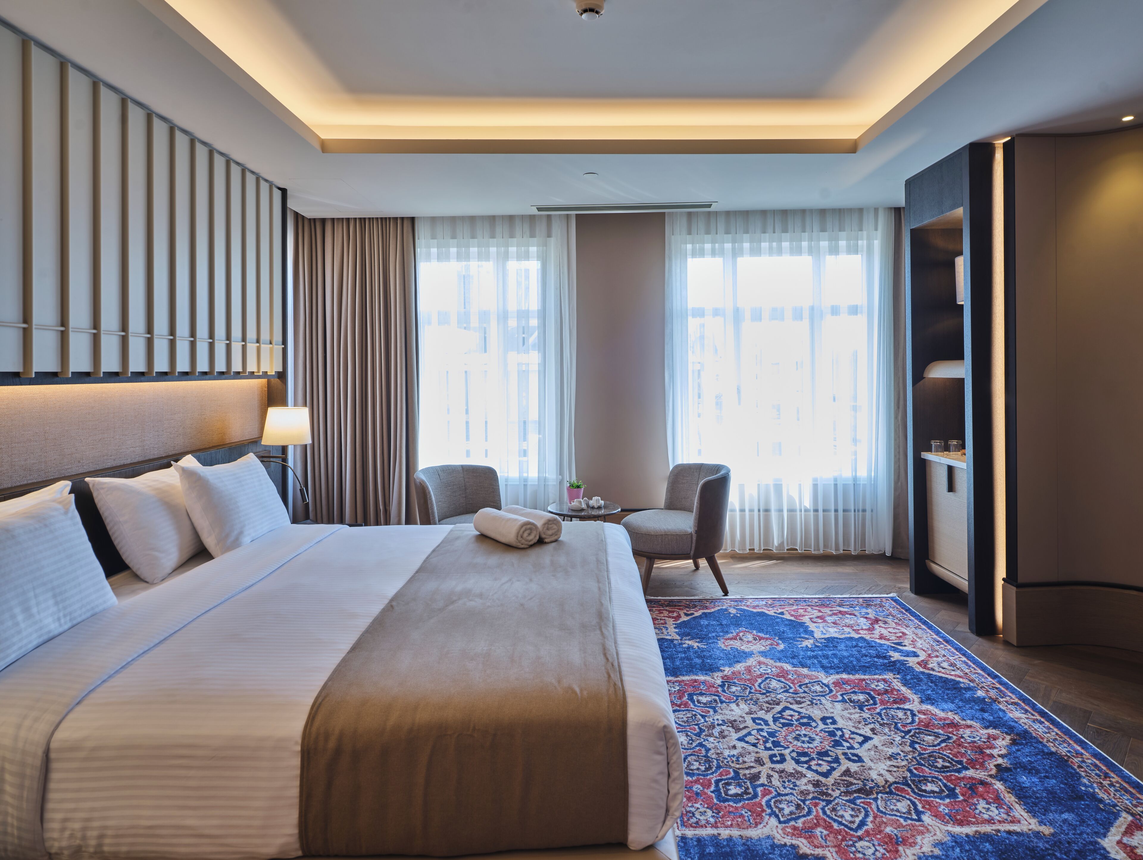 Een hotelkamer met een groot bed, een bureau, een stoel, een klein tafeltje en een kledingkast.