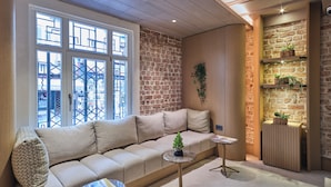 A modern living room with a beige sectional sofa, a small round table, and a built-in brick wall with shelves holding potted plants. - Four - G Hotel Premium (İstanbul)