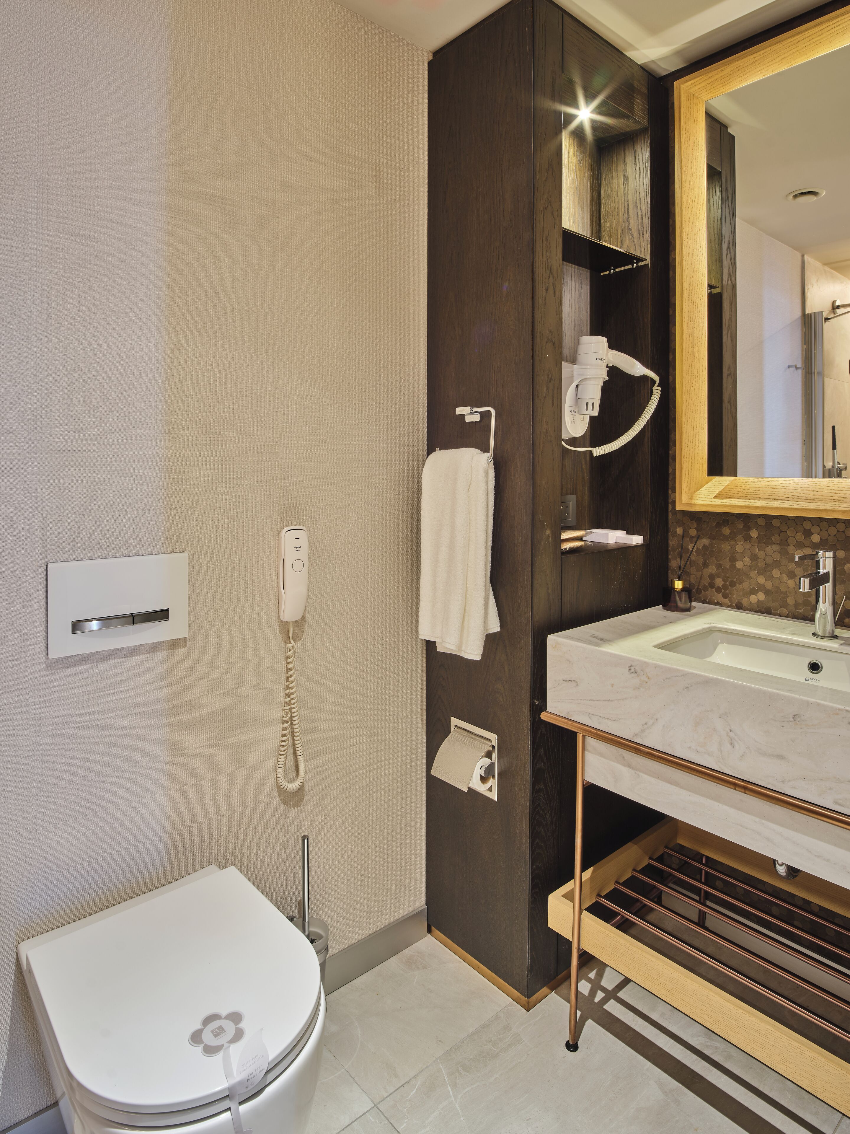 A modern bathroom with a toilet, a sink, a mirror, and a hairdryer.