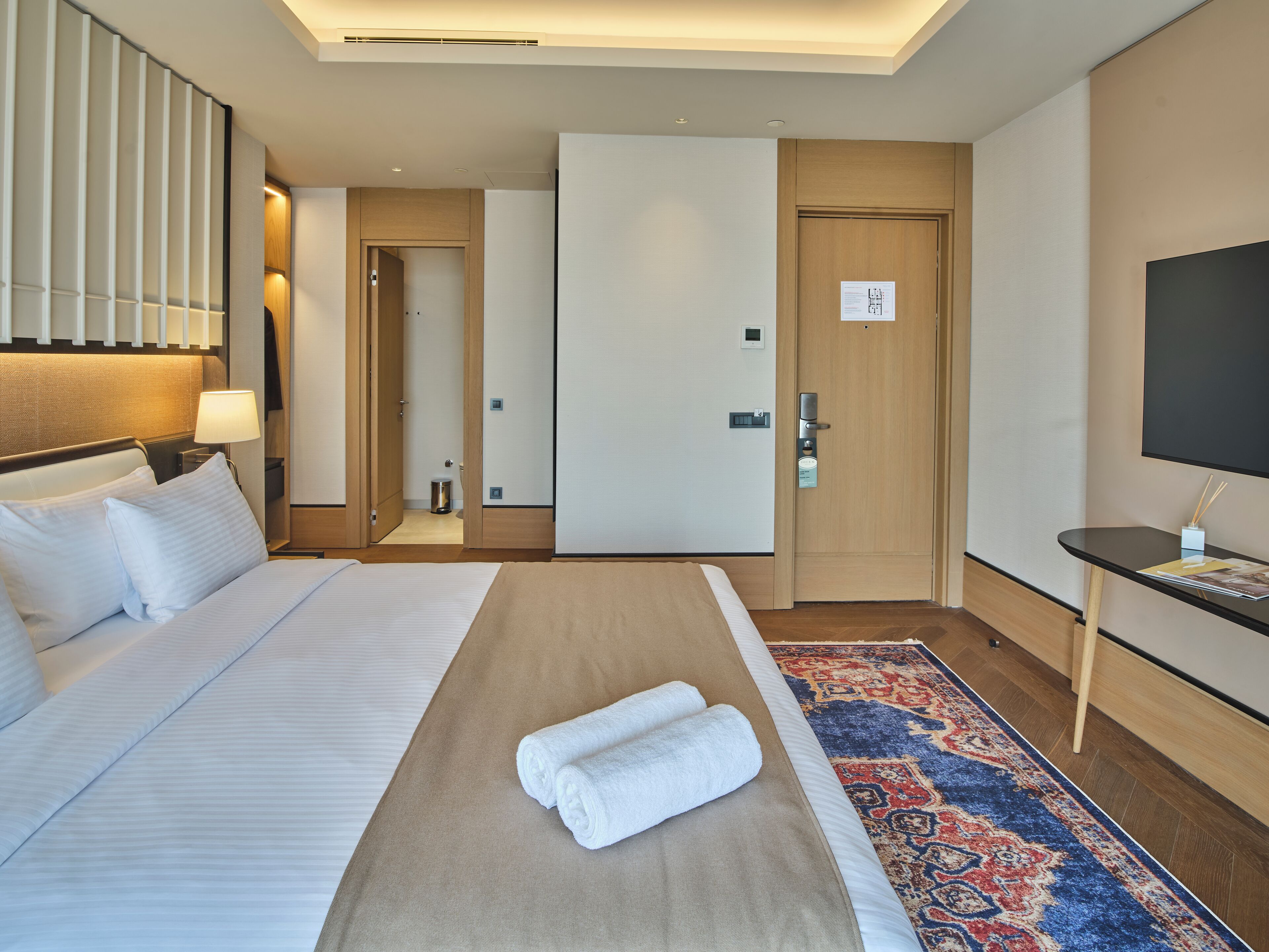 A hotel room with a bed, a TV, a desk, and a bathroom door.