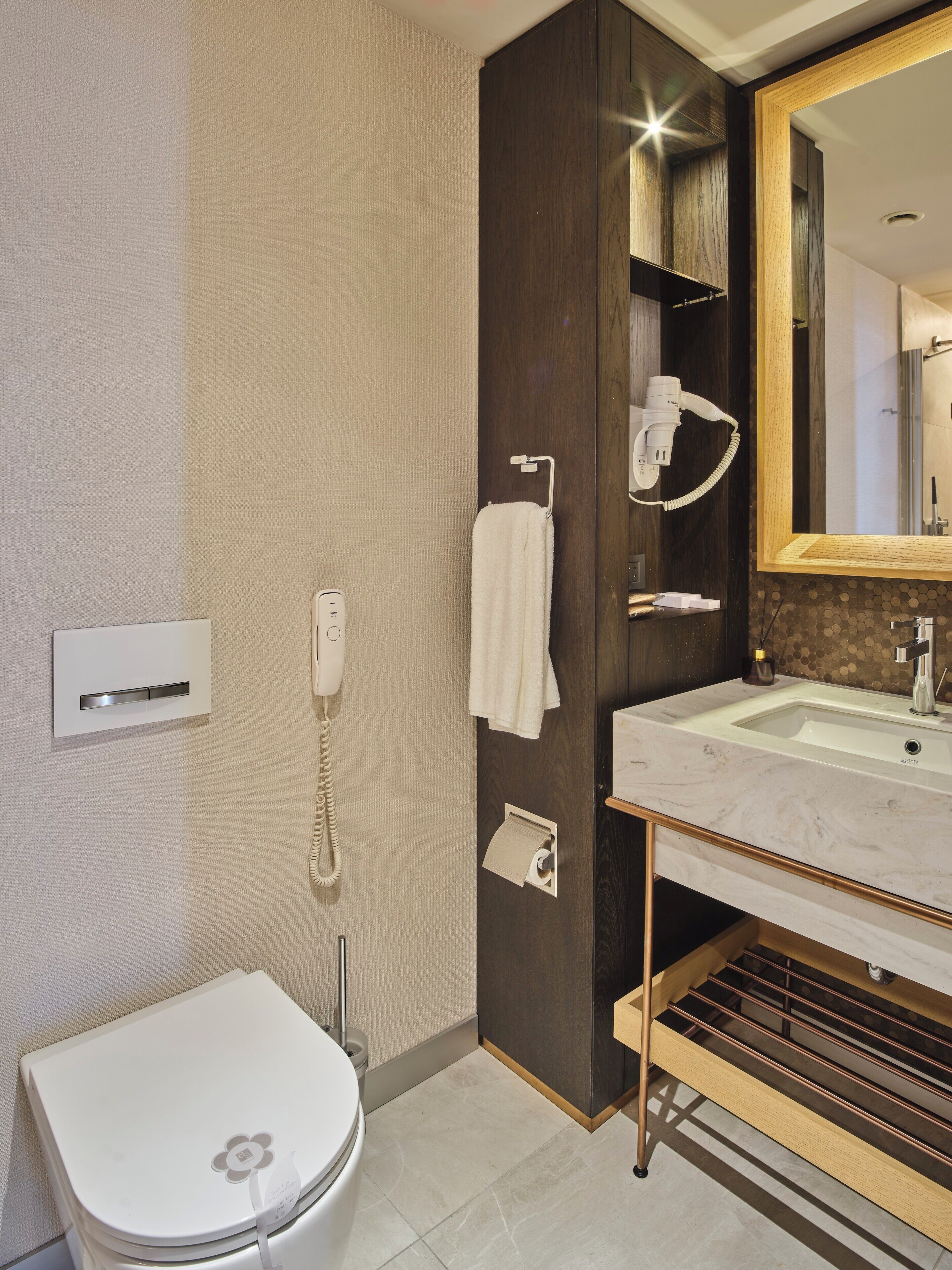 A modern bathroom with a toilet, a sink, a mirror, a hairdryer, and a telephone.