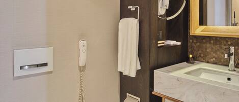 A modern bathroom with a toilet, a sink, a mirror, a hairdryer, and a telephone.
