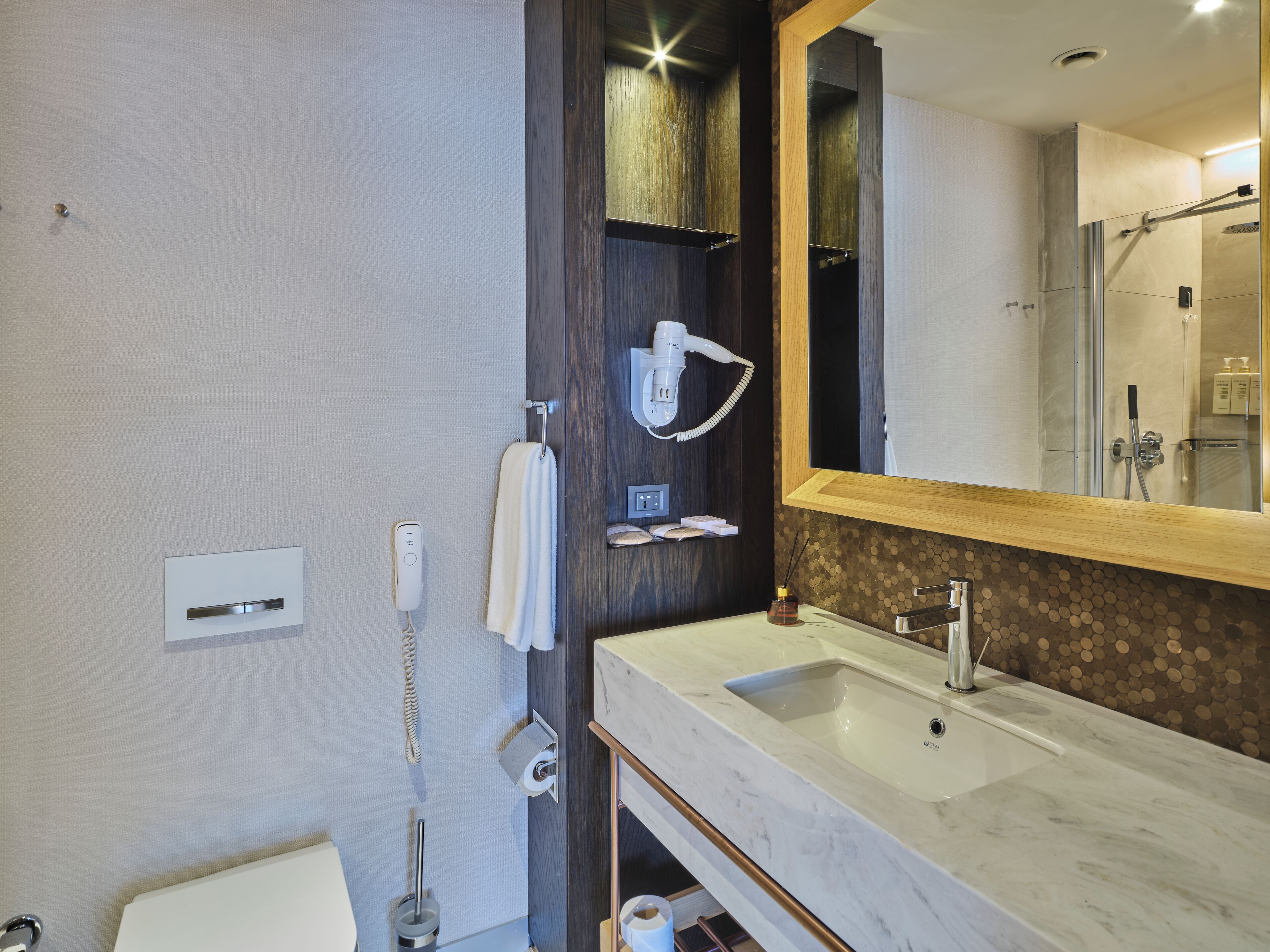 Uma casa de banho moderna com um espelho grande, uma pia, um secador de cabelo e uma sanita.
