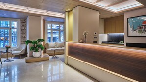 A modern reception area with a wooden reception desk, a sofa, a coffee table, and a potted plant. - Four - G Hotel Premium (İstanbul)