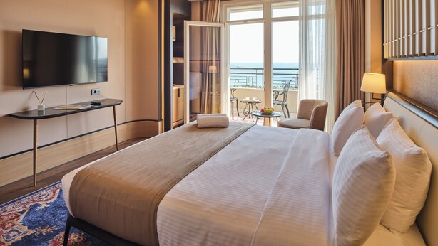 A hotel room with a large bed, a flat-screen TV, a desk with a lamp, and a balcony with a view of the sea. - Four - G Hotel Premium (İstanbul)