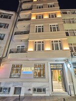 Ein mehrstöckiges Hotel mit einem markanten Eingang, einem Schild, das auf ein gehobenes Haus hinweist, und einer Treppe zum Eingang.