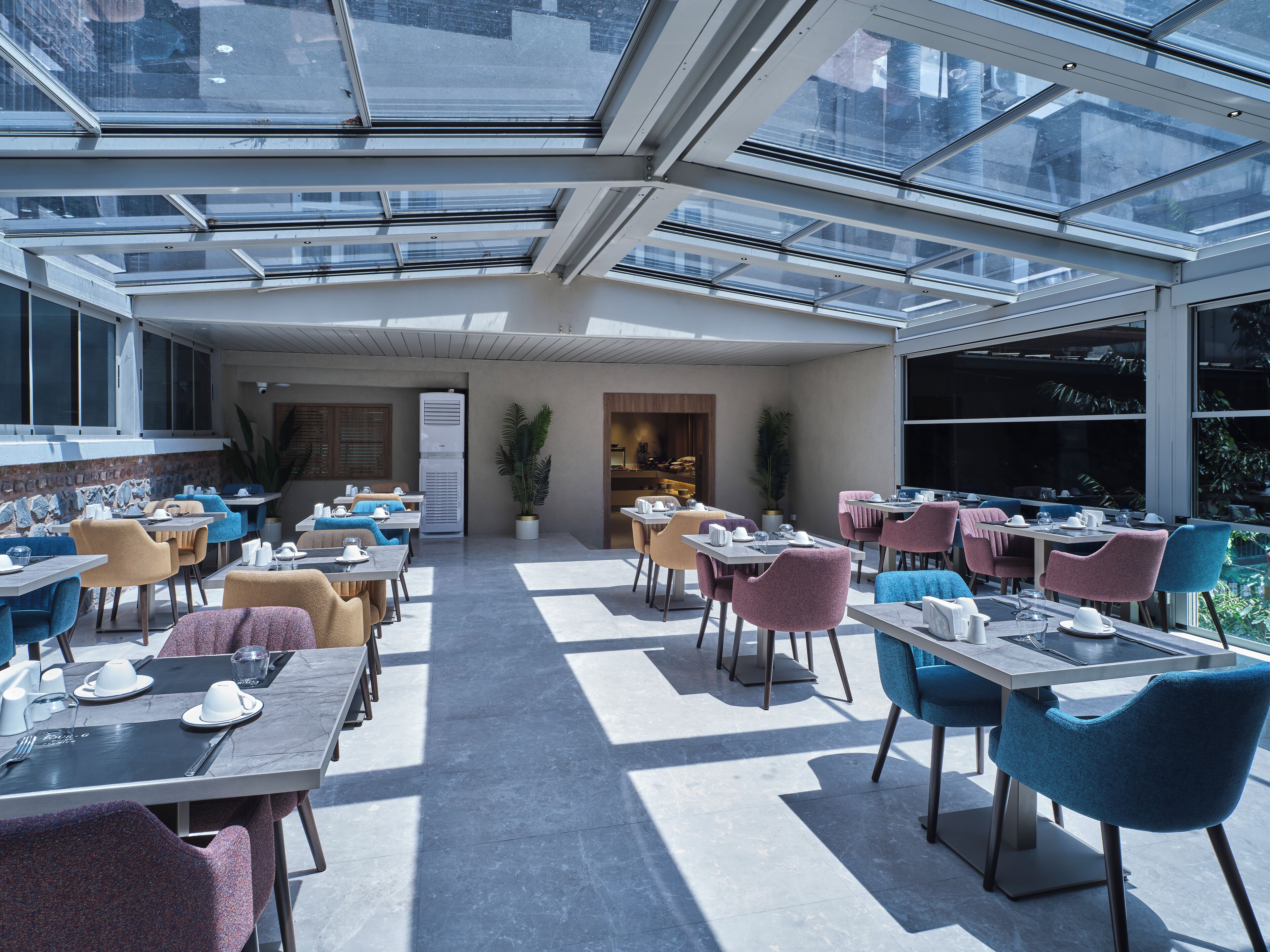 A modern outdoor dining area with glass ceilings, multiple tables, and chairs.