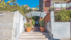 Un sendero estrecho que conduce a la entrada de un edificio, bordeado por macetas y un arco de metal.