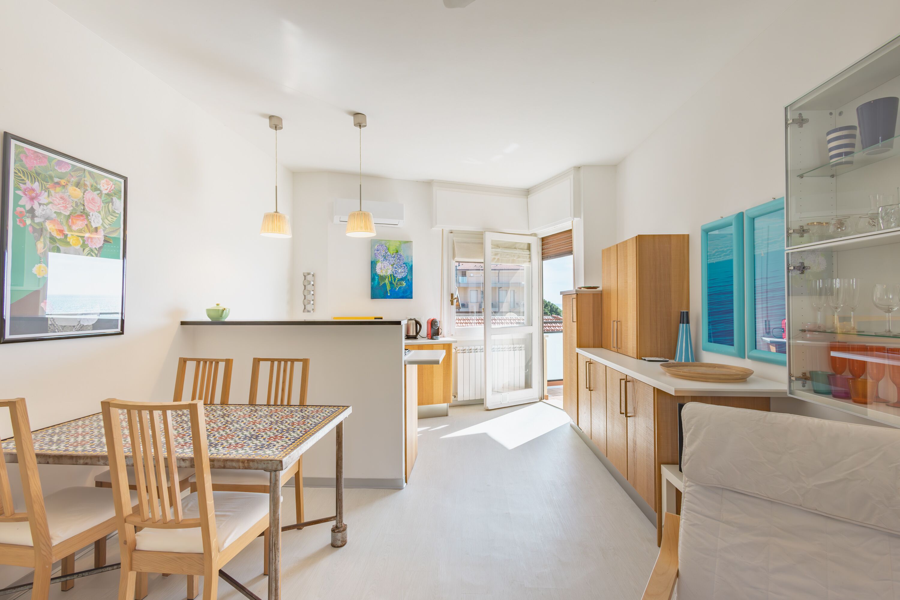 A modern kitchen with wooden cabinets, a dining table with chairs, and pendant lights.