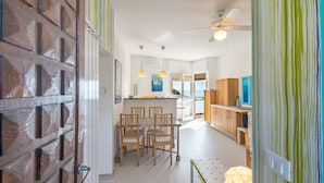 Una cocina moderna con armarios de madera, un comedor con mesa y sillas, y vista al mar a través de la puerta abierta.