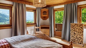 A bedroom with a wooden bed, a hanging light fixture, a wooden cabinet, and a view of the outdoors. - Chalet 'Glosaleite Zillertal' with Mountain View, Private Terrace and Wi-Fi (Zellberg)