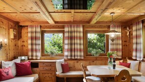 A wooden cabin interior with a dining table, bench seating, and a window with curtains. - Chalet 'Glosaleite Zillertal' with Mountain View, Private Terrace and Wi-Fi (Zellberg)