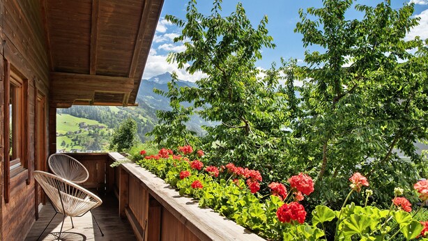 A wooden deck with a chair, a wooden railing, and a view of green hills and mountains. - Chalet 'Glosaleite Zillertal' with Mountain View, Private Terrace and Wi-Fi (Zellberg)