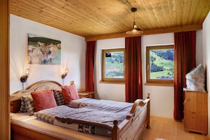 A wooden ceiling, a bed with a headboard, two windows with curtains, and a wall-mounted picture.