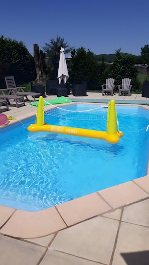 A swimming pool with inflatable floats, lounge chairs, and a tiled deck.