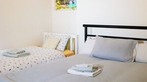 A hotel room with two beds, each with a white bedspread and pillows, and a painting of a coastal scene on the wall. - Triple Room in Kensington with Ensuite Bathroom and Workspace (Kensington)