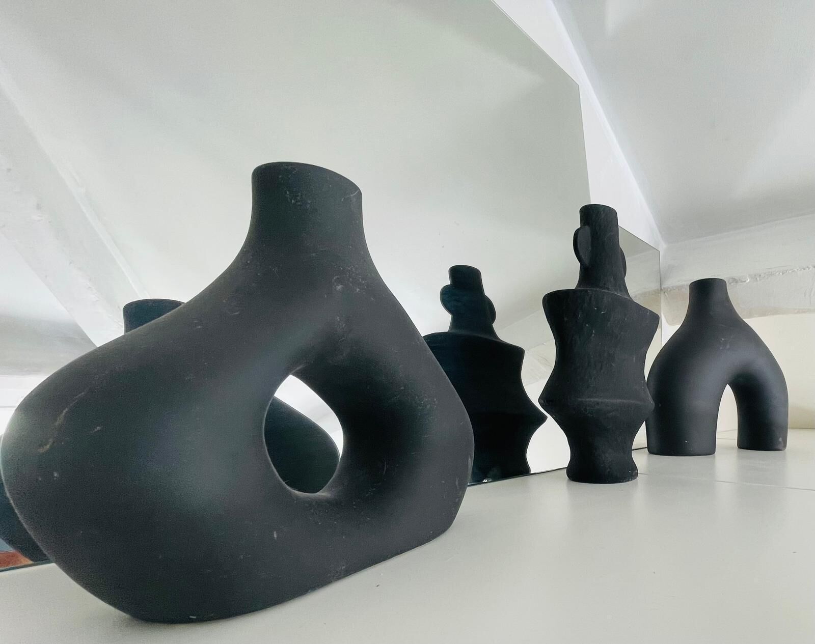 Un conjunto de esculturas negras y abstractas sobre un suelo blanco.