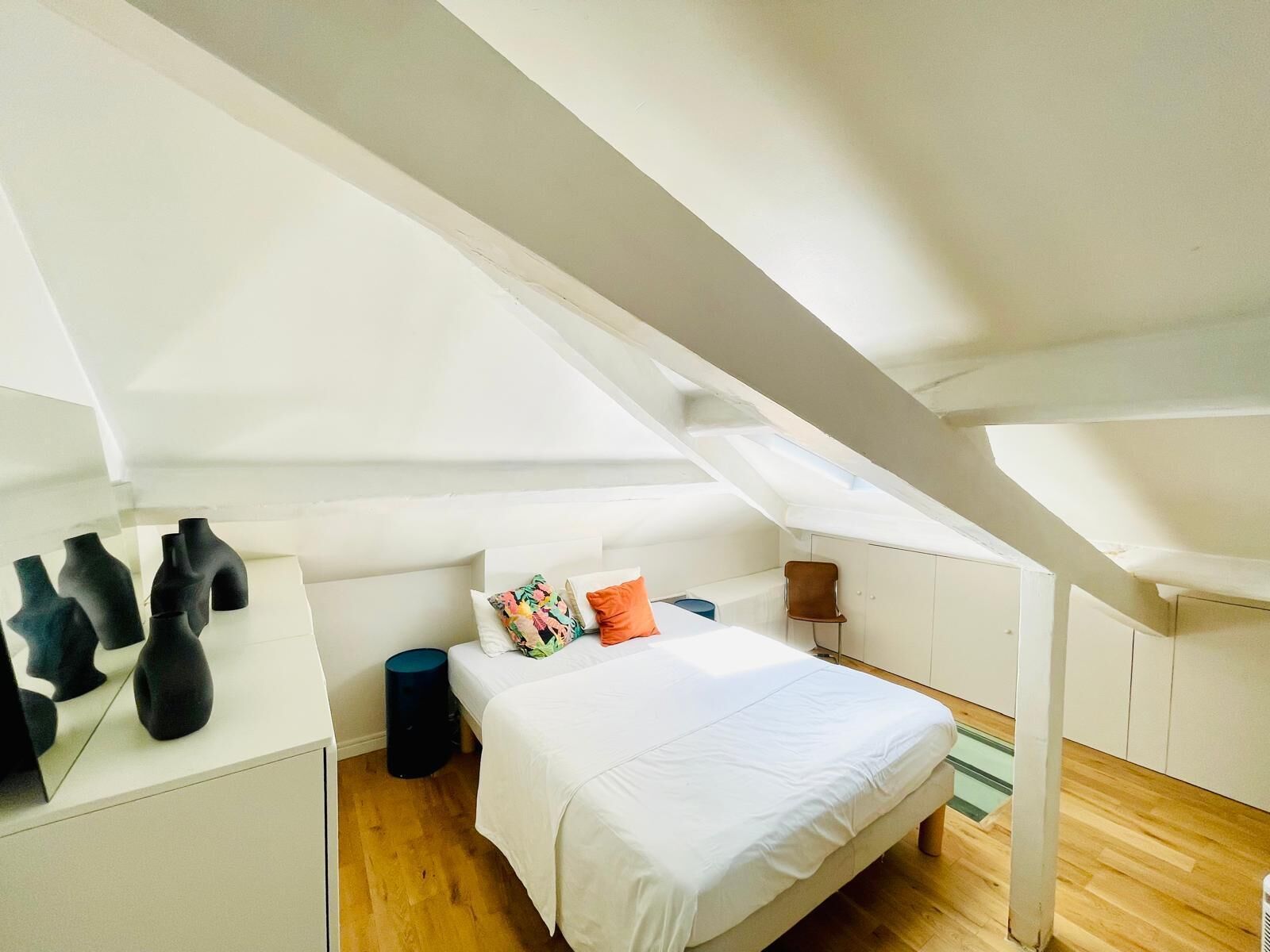 A bedroom with a sloped ceiling, a bed with white bedding, a small round table, and a chair.