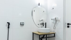 Une salle de bain moderne avec des toilettes blanches, un lavabo avec un miroir et une douchette à main.