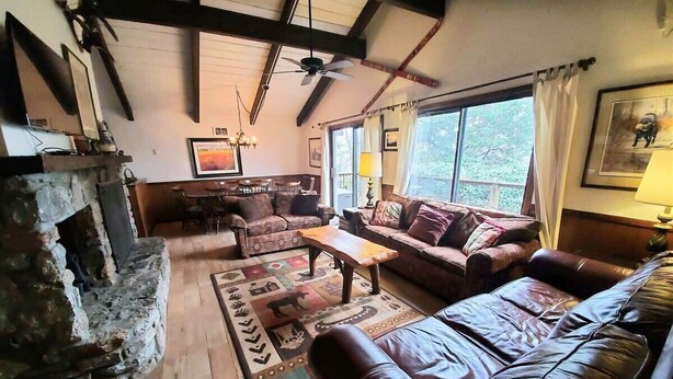 A rustic living room with a stone fireplace, leather sofas, and a large window with curtains. - CR-22 Harbeson Haven Peaceful 4 BR Chalet-Style Home Very well maintained (Beech Mountain)