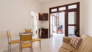 A living room with a beige sofa, a glass coffee table, and yellow chairs. There is a kitchen area with cabinets and a TV in the background. - 5 minutes from Copacabana beach | NSC906 (Rio de Janeiro)