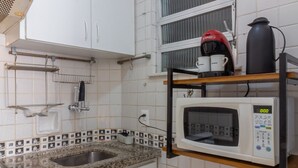 A small kitchen with white cabinets, a granite countertop, a microwave, and a window with blinds. - 5 minutes from Copacabana beach | NSC906 (Rio de Janeiro)