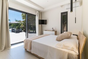 A modern bedroom with a large bed, a TV mounted on the wall, and a sliding glass door leading to an outdoor area. - Nereide, luxury villa in Sicily with pool, near the beach (Punta Secca)