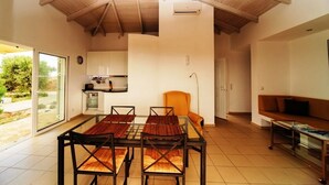 Amplia sala de estar con techo alto, una mesa de comedor con cuatro sillas, un sofá y una cocina al fondo.