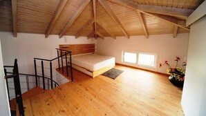 Un dormitorio estilo ático con techos altos, piso de madera, una cama, un ventanal y una escalera.