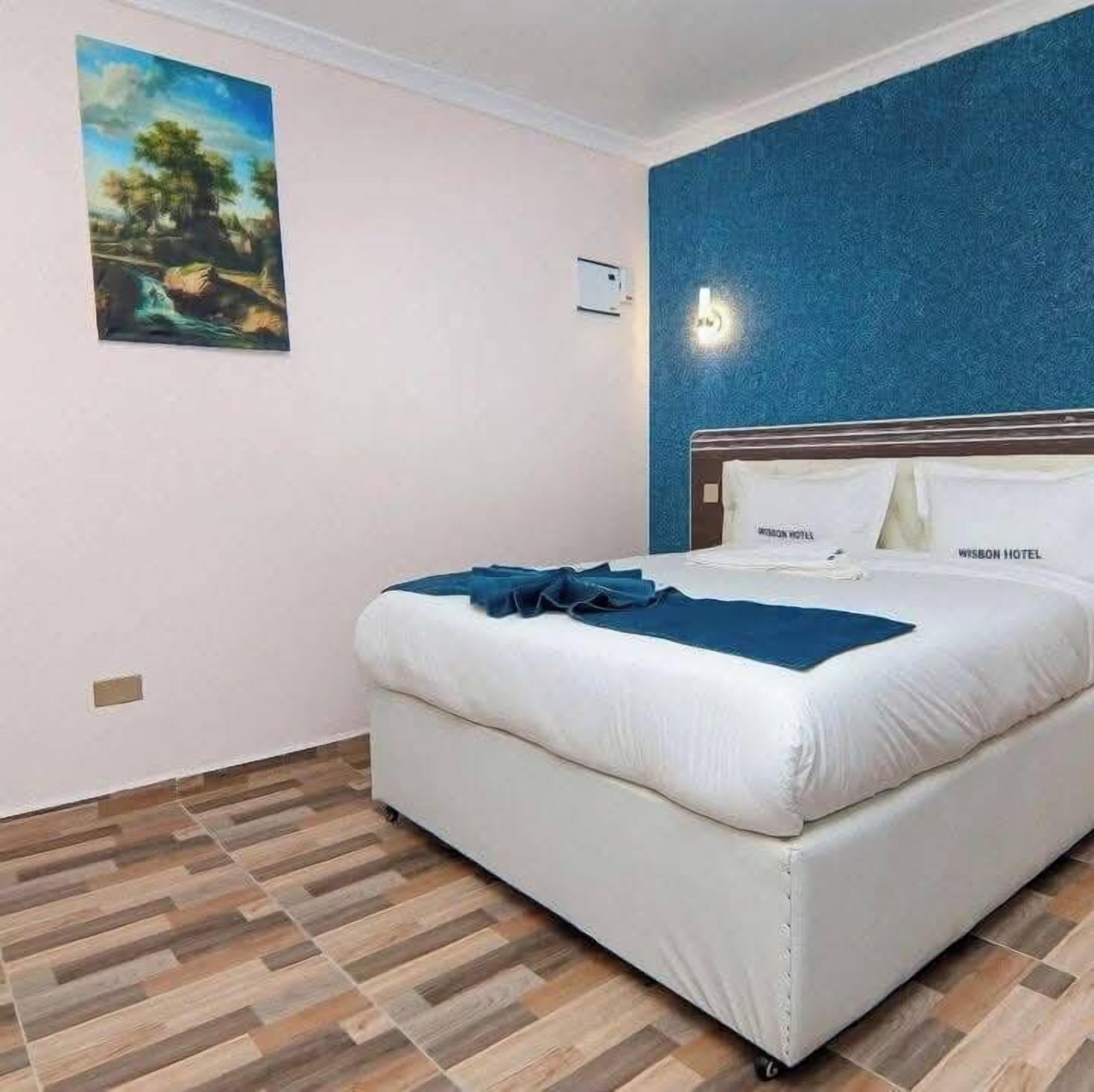 Una habitación de hotel con una cama, un cuadro en la pared y una pared azul con textura.